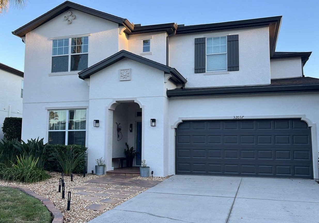 Two-story white stucco home with dark trim, shutters, and garage door, featured on the About Top Banana Painting page.
